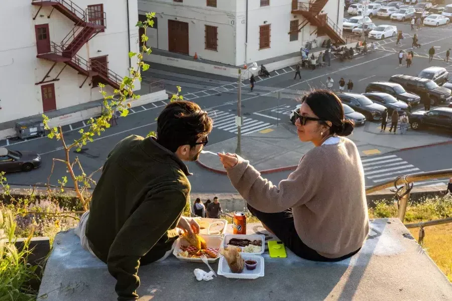 Ein Paar speist im Freien im Fort Mason Center in San Francisco. Die Frau gibt ihrem Begleiter eine Kostprobe.