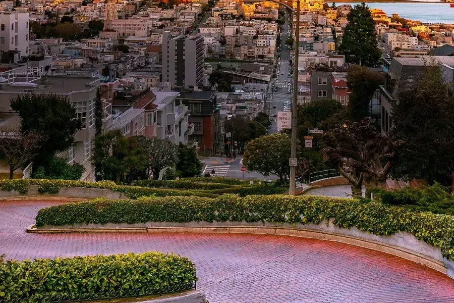 Lombard Street se curva con Coit Tower en la distancia durante sunset .