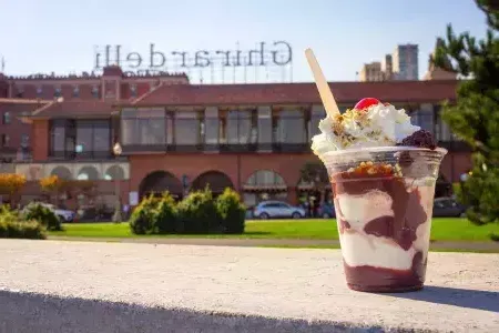 Un helado de chocolate se encuentra en primer plano con la plaza Ghirardelli al fondo.